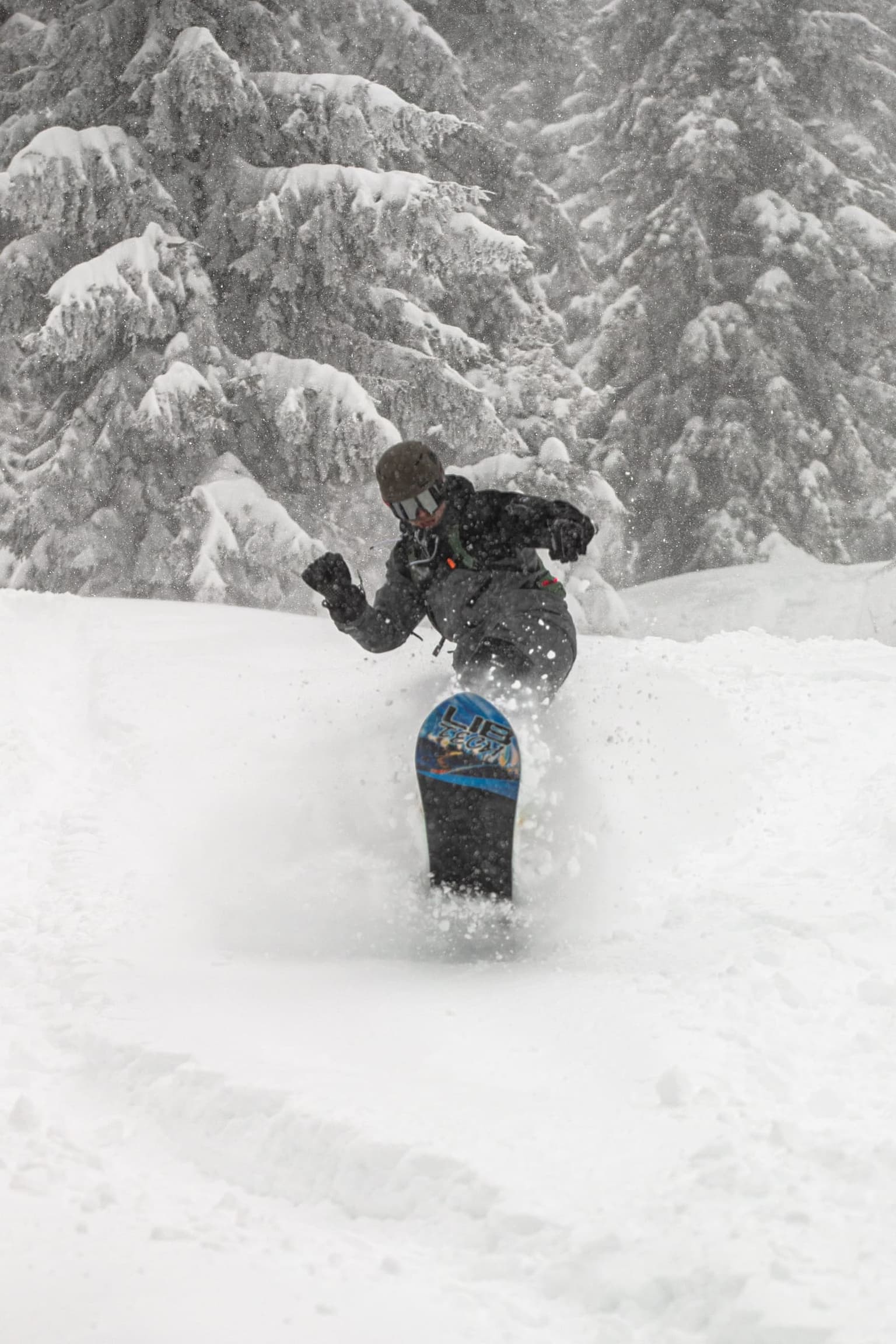 Snowboarder carving through deep snow in a forested section.