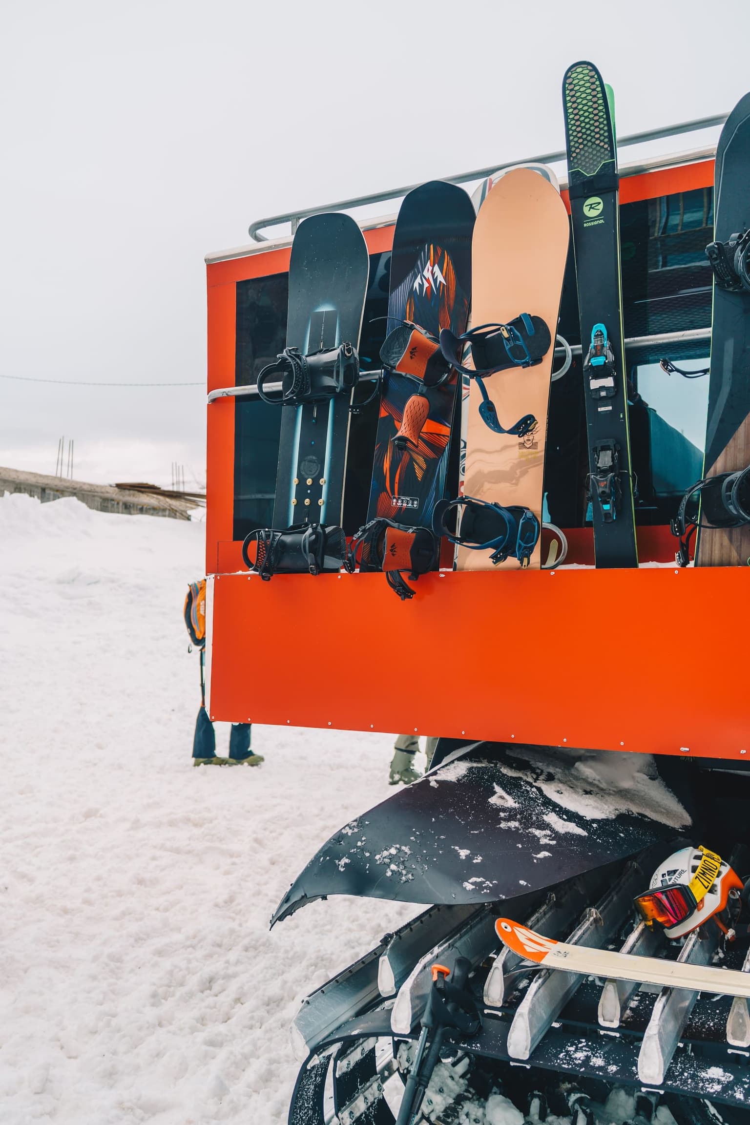 Snowboards lined up on the side of a bright orange snow vehicle.